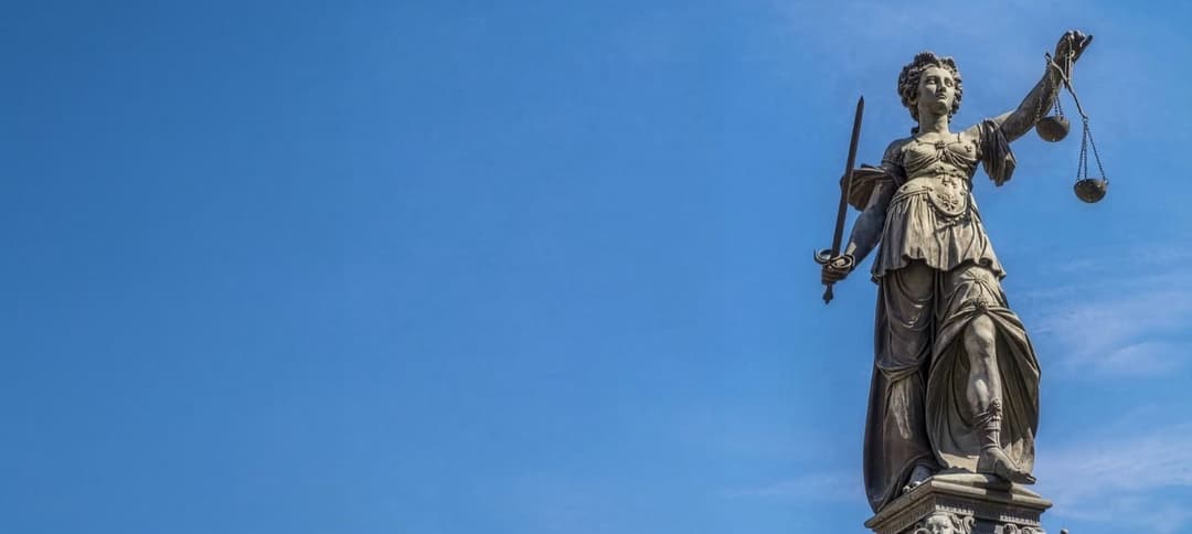Açık mavi gökyüzü önünde, sağ tarafta elinde terazi ve kılıç tutan Justitia heykeli